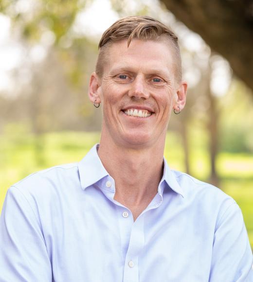 Alex Nord smiling wearing a light blue long sleeve button up in nature
