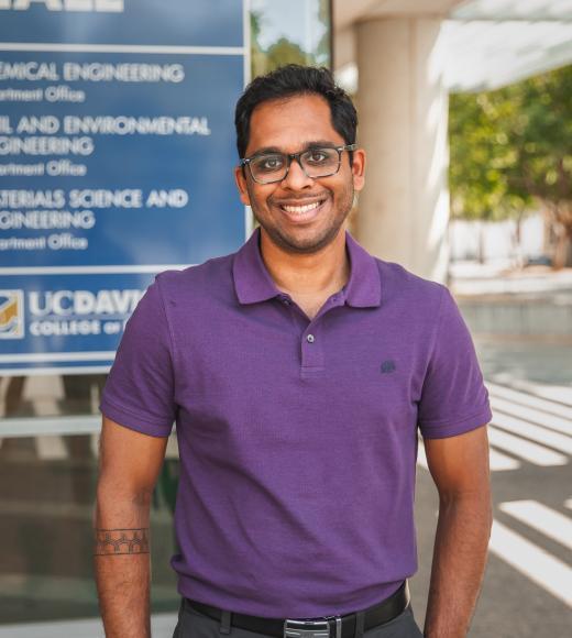 A headshot of Ambar standing in front of his office building wearing a purple polo.