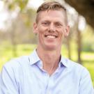 Alex Nord smiling wearing a light blue long sleeve button up in nature